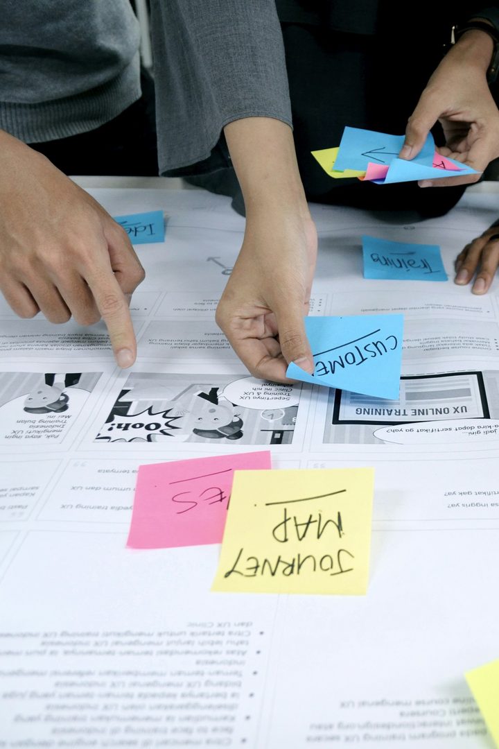 Des mains autour d'une grande feuille couverte de post-it, pendant un atelier de travail