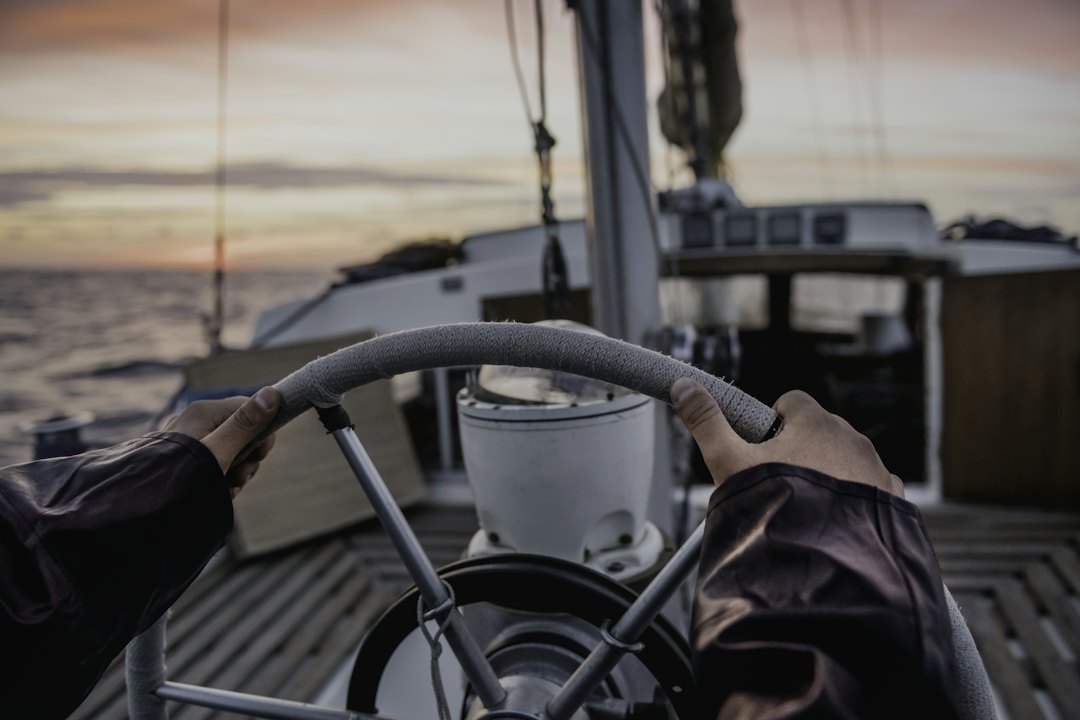 Deux mains sur la barre à roue d'un voilier, vue du barreur