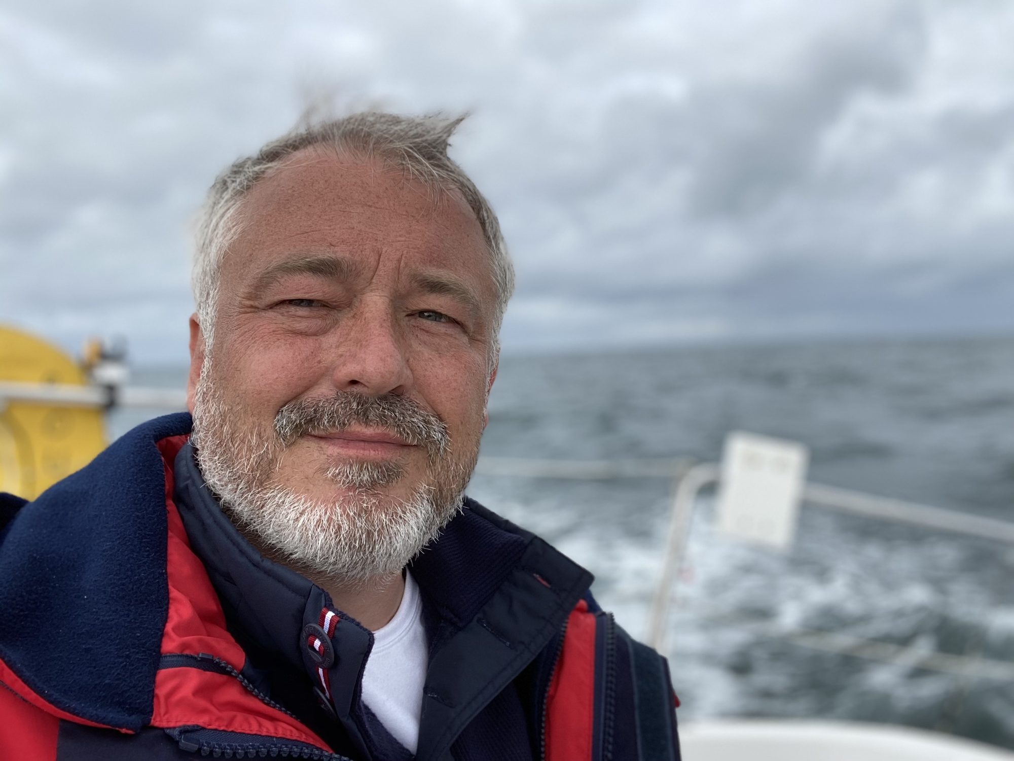 Raphaël Hélion en mer, sur l'arrière d'un voilier, ciel couvert